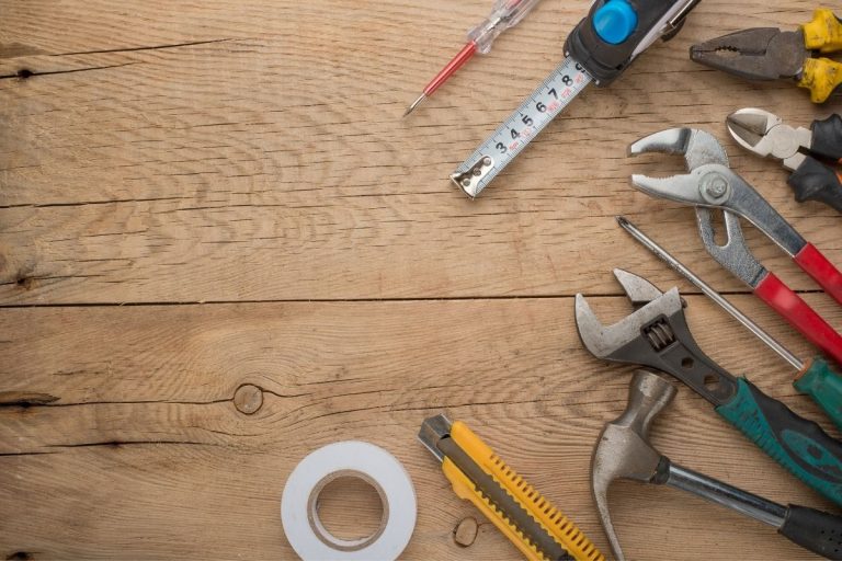 A variety of tools, including a hammer and screwdriver, arranged neatly on a wooden table surface.