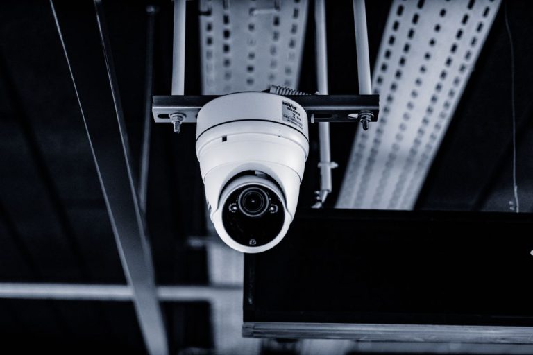 A ceiling-mounted security camera with a rounded white casing, capturing surveillance in a dimly lit environment.