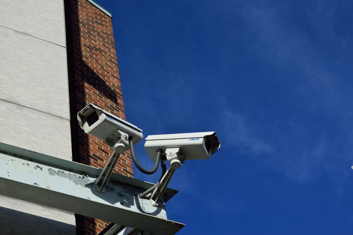 Two security cameras mounted on a building against a clear blue sky, highlighting surveillance and monitoring features.