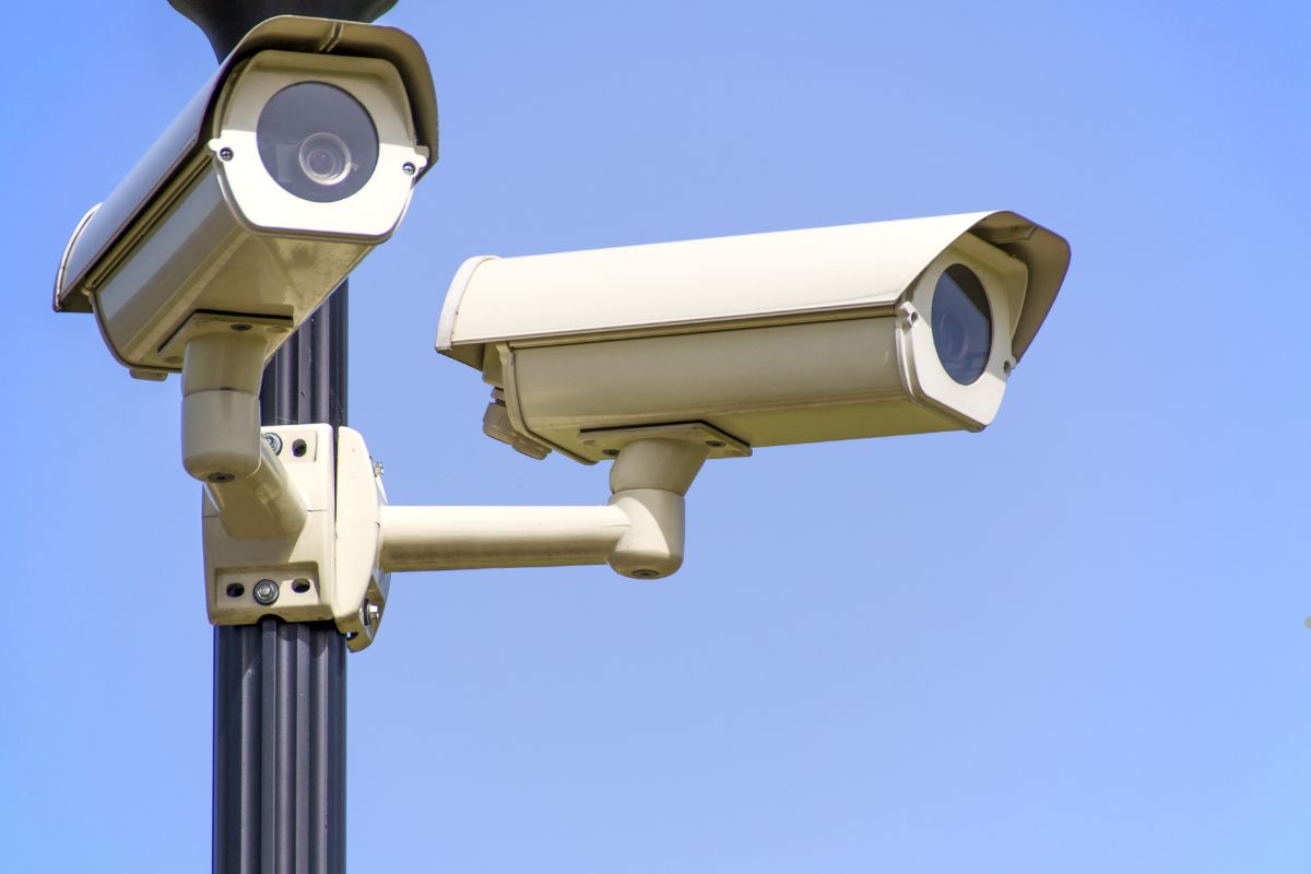 Two security cameras mounted on a pole against a clear blue sky, highlighting surveillance and safety features.